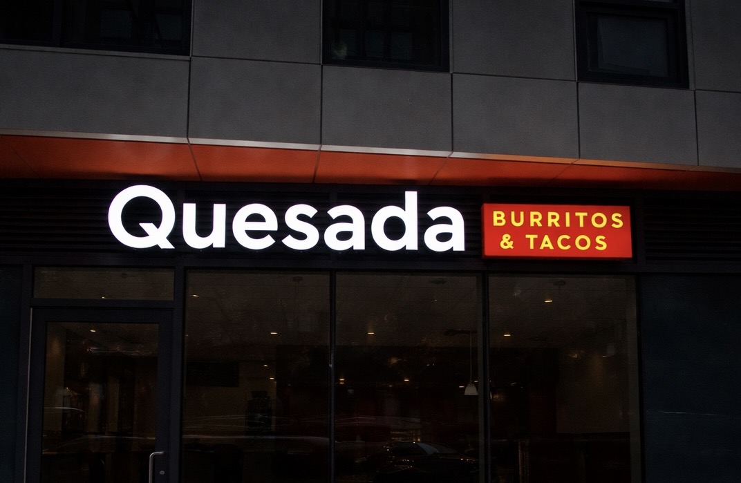 Quesada Burritos & Tacos — clean white front-lit letters with illuminated logo cabinet